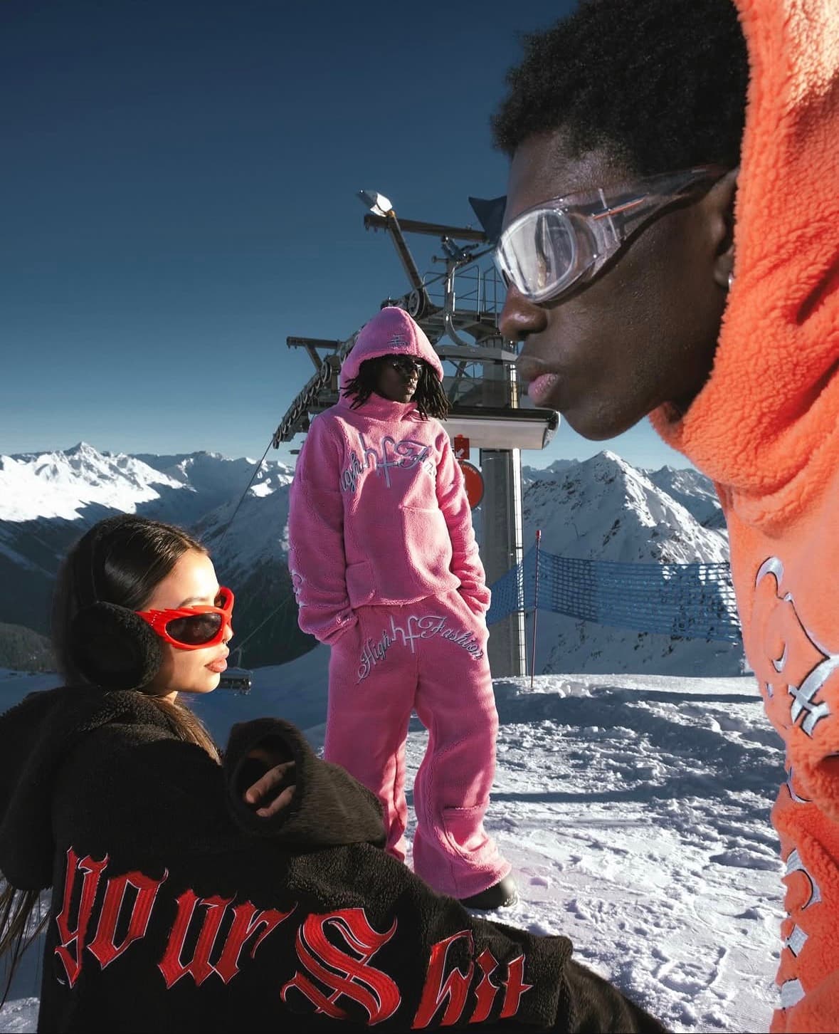 Models in orange, pink, and black fleece streetwear posing on a snowy mountain peak.